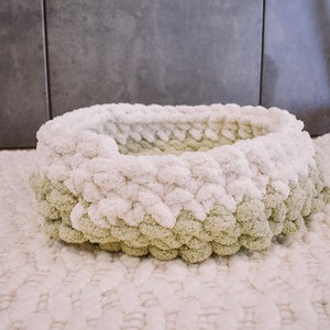 May include: A white and green knitted pet bed with a round shape. The bed is made of fluffy yarn and has a soft, cozy texture.