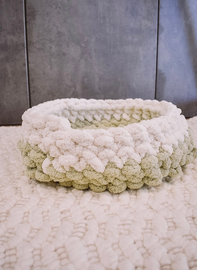 May include: A white and green knitted pet bed with a round shape. The bed is made of fluffy yarn and has a soft, cozy texture.