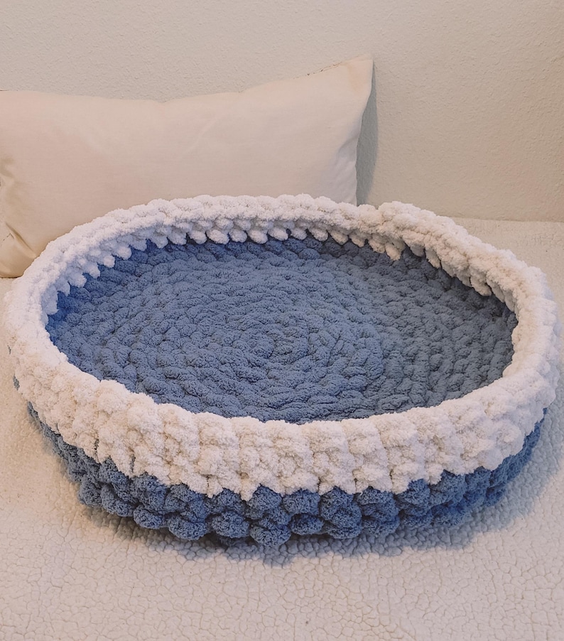 May include: A blue and white crocheted pet bed. The bed is round and has a white rim.
