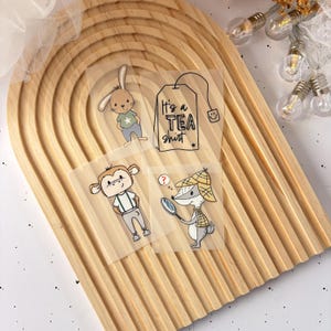 Könnte beinhalten: Vier transparente Aufkleber mit Illustrationen eines Hasen, eines Affen, eines Waschbären und eines Teebeutels mit dem Text "It's a Tea Shirt".