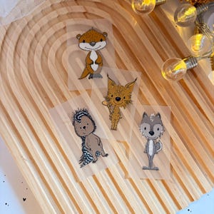 Könnte beinhalten: Vier illustrierte Tieraufkleber auf transparentem Hintergrund. Die Tiere sind ein brauner Otter, ein braun-weißer Luchs, ein brauner Igel und ein grauer Wolf.