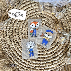 Könnte beinhalten: Drei Bügelbilder mit Cartoon-Tieren in Arbeitskleidung. Die Designs zeigen einen Fuchs in einem blauen Overall mit einem Schraubenschlüssel, einen Waschbären in einem blauen Overall mit einem Schraubenschlüssel und einen Biber in einem blauen Overall mit einer Bohrmaschine. Der Text "mini Bügelbild" ist auf einem weißen Etikett sichtbar.