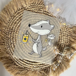 Könnte beinhalten: Ein Druck mit einem Cartoon-Dachs, der eine Laterne mit einem Sterndesign hält. Der Dachs ist grau und weiß, mit einer gelben und blauen Laterne. Ein kleinerer Dachs mit einer Laterne befindet sich im Hintergrund. Der Hintergrund ist hellbraun mit einem kreisförmigen Muster.