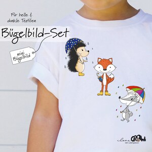 Könnte beinhalten: Weißes T-Shirt mit Bügelbild-Set von Tieren: ein Igel, ein Fuchs und ein Dachs, jeder mit einem Regenschirm. Der Text "Bügelbild-Set" und "mini Bügelbild" sind sichtbar. Für helle und dunkle Textilien.