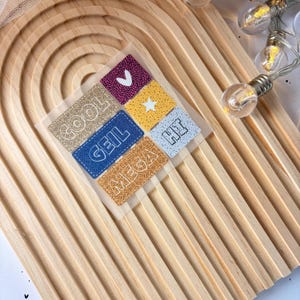 Könnte beinhalten: Ein Set mit sechs bunten Aufklebern mit verschiedenen Wörtern und Designs. Die Aufkleber befinden sich auf einer Holzoberfläche. Die Wörter auf den Aufklebern sind "cool", "geil", "mega", "hit" und ein Herz.