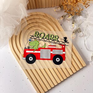 Könnte beinhalten: Ein rotes Feuerwehrauto mit einem grünen Dinosaurier-Fahrer. Das Auto hat eine Leiter und das Wort "ROARR" steht an der Seite. Der Dinosaurier trägt einen blauen Hut.