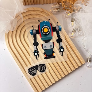 Könnte beinhalten: Ein blauer und roter Roboter mit einem gelben Auge und dem Text "COOL BOY" auf einem transparenten Aufkleber. Der Aufkleber befindet sich auf einer Holzoberfläche.