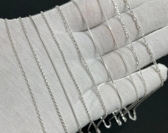 May include: A collection of silver chains of different styles and thicknesses, displayed on a white surface.