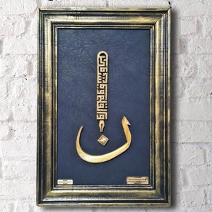 Könnte beinhalten: Ein gerahmtes Stück islamischer Kalligrafiekunst mit goldenen Buchstaben auf dunkelblauem Hintergrund. Die Kalligrafie hat die Form eines einzelnen Buchstabens, der von einem dekorativen Rahmen umgeben ist. Der Rahmen ist aus Holz und hat eine goldene Oberfläche.