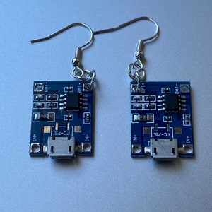 May include: A pair of unique earrings made from small, rectangular blue circuit boards. Each board has silver-colored metal ear wires and features electronic components, including a USB port and the text "FC-75."