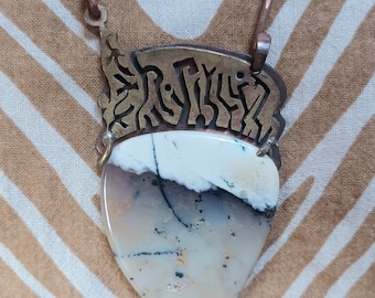 May include: A white and gray agate pendant with black veins, set in a brass frame with an intricate design. The pendant is attached to a brass chain.