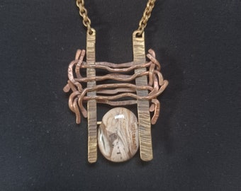 May include: A brass and copper necklace with a geometric design and a round, brown and white agate stone pendant.