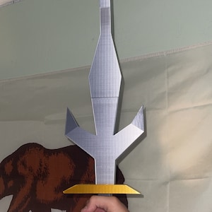 May include: A silver-colored, three-pronged sword with a gold-colored handle. The sword is held by a hand in front of a California state flag.