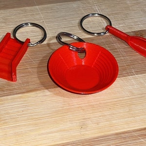 May include: Three red plastic keychain charms: a small bowl, a paddle, and a set of stairs. The charms are attached to silver key rings.
