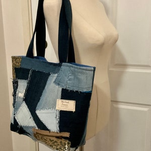 May include: A blue denim tote bag with a patchwork design. The bag has a zippered pocket and a label that says "This band forever".