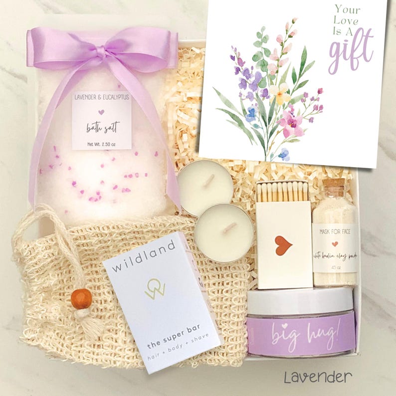 May include: A gift box with lavender and eucalyptus bath salt, a card with floral art, two tea lights, matches, a face mask, a jar of cream with "big hug!" text, and a soap bar. The box is tied with a lavender ribbon.