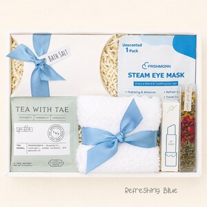 Puede incluir: Una caja de regalo que contiene una caja tipo almohada blanca con una cinta azul etiquetada como sal de ba&ntilde;o, una m&aacute;scara de vapor para ojos Frshmorn, un sobre de t&eacute; herbal Tea With Tae, una toalla blanca con cinta azul, un b&aacute;lsamo labial y un tubo con flores secas.