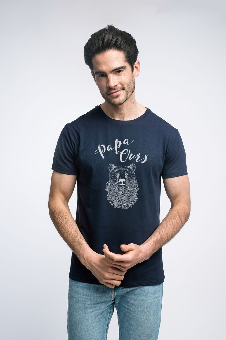May include: A navy blue t-shirt with a white graphic of a bear with a beard and moustache. The text "Papa Ours" is printed above the bear.