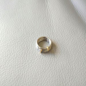May include: A silver ring with three bands and two small gold accents.