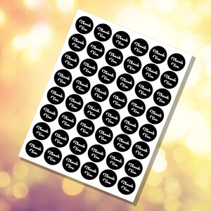 May include: A sheet of white paper with 49 black and white round stickers. Each sticker has the text "Thank You" in a white cursive font.