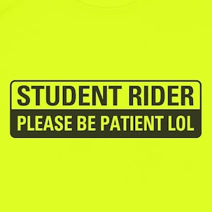May include: A neon yellow t-shirt with a black rectangular graphic. The graphic reads "STUDENT RIDER PLEASE BE PATIENT LOL" in white capital letters. The shirt is a solid color with a crew neck.