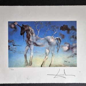 May include: A surrealist print featuring a unicorn with tree-like structures growing from its back, set against a blue sky with clouds. The artwork includes a signature and the date 1977. The print is on textured paper.