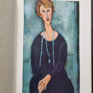 May include: A print of a painting featuring a woman with red hair and a long neck, wearing a black dress and a turquoise beaded necklace. The background is a teal color. The artist's name, Modigliani, is in the upper right corner.