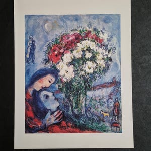 Pode incluir: Uma pintura de Marc Chagall que retrata um casal abraçando-se em frente a um grande buquê de flores vermelhas, brancas e rosadas. O fundo apresenta um céu azul com uma lua crescente e uma pequena aldeia.