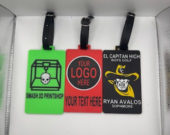 May include: Three luggage tags with black straps. One is green with a 3D printer and skull graphic, the text "SMASH 3D PRINT SHOP". The second is red with "YOUR LOGO HERE" and "YOUR TEXT HERE". The third is black with "EL CAPITAN HIGH BOYS GOLF" and "RYAN AVALOS SOPHMORE".