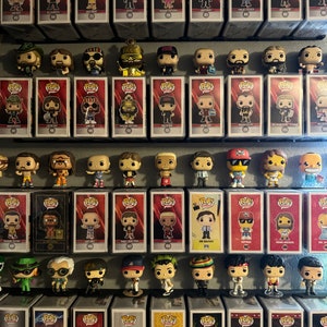 May include: A collection of colourful pop culture figures displayed on a black shelf. The figures are in protective plastic cases with red and white labels. The figures are arranged in rows and columns. The figures are all different characters from popular films, TV shows, and video games.
