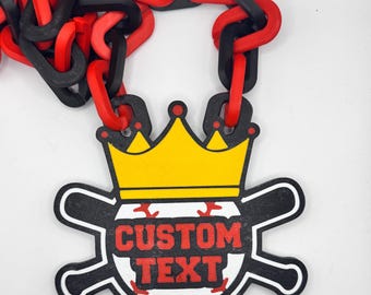 May include: A black, red, and yellow baseball-themed necklace. The pendant features a yellow crown, a baseball design, and the words "CUSTOM TEXT" in red. The chain is made of alternating red and black links.