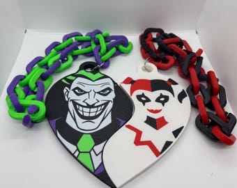 May include: Two heart-shaped pendants featuring comic book characters, the Joker and Harley Quinn. The Joker pendant is black with green and purple accents, while Harley Quinn is white with red and black details. Each pendant has a chain of matching colors.