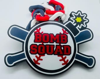 May include: A white baseball with red stitching and the words "Bomb Squad" in red letters. The baseball is surrounded by two blue and white baseball bats and a red, white, and blue chain. A yellow star with a white outline is in the upper right corner.