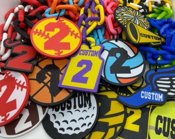 May include: A variety of colorful plastic chains with charms featuring different sports and the number "2" on them. The charms include a baseball, basketball, volleyball, golf ball, soccer ball, and a running shoe. The charms also have the word "CUSTOM" on them.