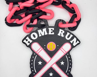 May include: A black and pink baseball-themed necklace. The pendant reads "HOME RUN" in white letters and features crossed bats, a baseball, and stars. The chain is made of alternating pink and black links.