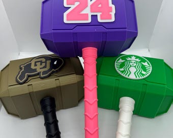 May include: Three colorful plastic toy hammers with different designs. The purple hammer has the number "24" on it. The green hammer has a Starbucks logo. The brown hammer has a brown and gold logo.