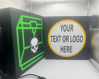 May include: Two black square signs. One features a neon green graphic of a 3D printer with a skull. The other sign has a white circle with yellow trim and the text "YOUR TEXT OR LOGO HERE" in black.
