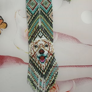 May include: A beaded necklace with a dog face design in the center. The necklace is made with green, blue, white, red, and black beads. The dog face is white with brown and black details. The necklace has a fringe of beads at the bottom.