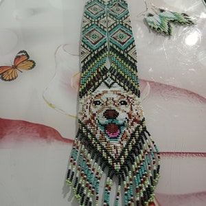 May include: A beaded necklace with a dog's face in the center, surrounded by geometric patterns in shades of green, blue, white, and black. The necklace has long fringe tassels in the same colors. Matching earrings are also included.