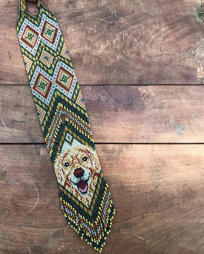 May include: A beaded necklace with a green, yellow, and white geometric pattern. The bottom of the necklace features a beaded image of a golden retriever dog.