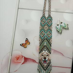 May include: A long beaded necklace with a geometric pattern and a beaded image of a golden retriever dog's face. The necklace has a fringe at the bottom and comes with matching beaded earrings.