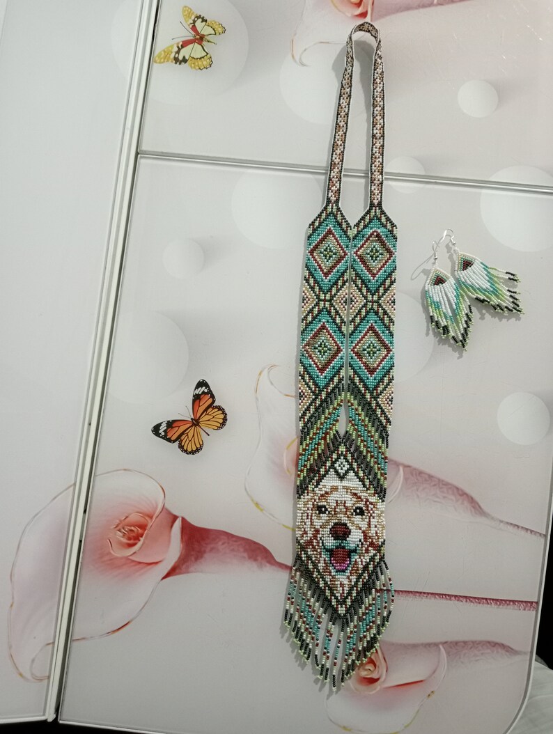 May include: A long beaded necklace with a geometric pattern and a beaded image of a golden retriever dog's face. The necklace has a fringe at the bottom and comes with matching beaded earrings.