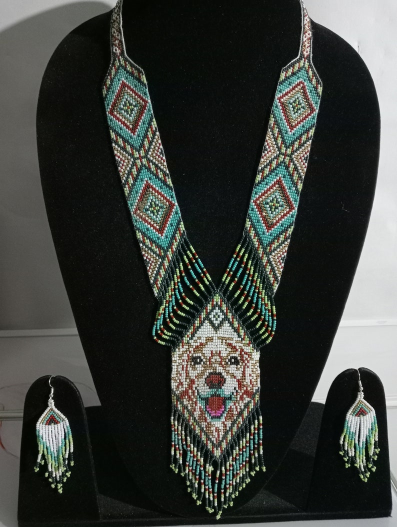 May include: A beaded necklace and earrings set with a dog's face in the center of the necklace. The necklace is made of black, white, green, red, and blue beads. The earrings are made of white, green, and blue beads.