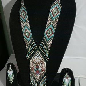 May include: A beaded necklace and earrings set featuring a dog's face in the center of the necklace. The necklace is made of black, white, green, red, and brown beads. The earrings are made of black, white, green, and light blue beads.