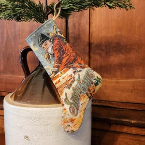 May include: A vintage-style Christmas stocking with a blue background and a picture of Santa Claus climbing down a chimney. The stocking has the text "Dear Santa Claus" on it.