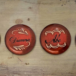 May include: Four round, red coasters with white and gold designs. The coasters feature a weeping willow tree, the names "Dianna" and "Abe", and the text "Est. 1963".