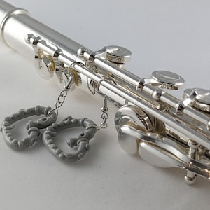 May include: A silver flute with two gray heart-shaped earrings attached to the keys.