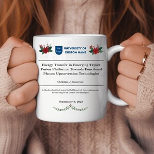 Puede incluir: Taza de cerámica blanca con un diseño navideño rojo y verde. La taza presenta el texto "University of Custom Name" y "Energy Transfer in Emerging Triplet Fusion Platforms: Towards Functional Photon Upconversion Technologies". También se incluye el texto "Christian J. Imperiale" y "September 9, 2023".