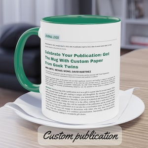May include: A white ceramic mug with a green handle and interior, resting on a white saucer. The mug features text from a publication, including the title "Celebrate Your Publication: Get The Mug With Custom Paper From Geek Twins". The words "Custom publication" are at the bottom.