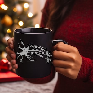 Könnte beinhalten: Schwarze Kaffeetasse mit einem weißen Neuronen-Motiv und dem Text "You've got potential".